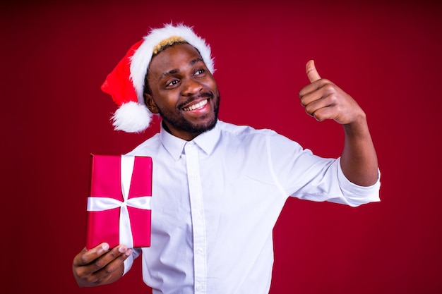 Hombre hispano latino con camiseta blanca con fondo rojo de estudio con una pequeña caja de regalos