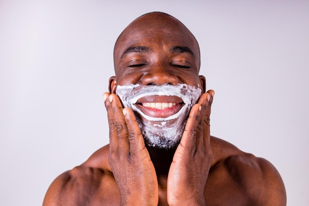 Hombre hispano latino con maquinilla de afeitar y espuma de afeitar en el fondo aislado blanco del estudio de la cara