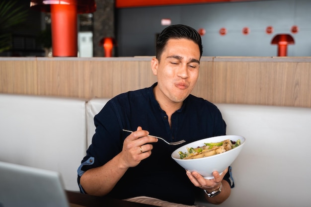 Hombre hispano masticando y comiendo ensalada durante el almuerzo en el trabajo