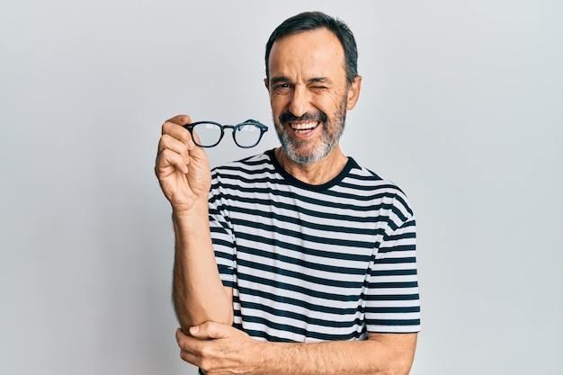 Hombre hispano de mediana edad con ropa informal y gafas guiñando un ojo mirando a la cámara con expresión sexy, cara alegre y feliz.