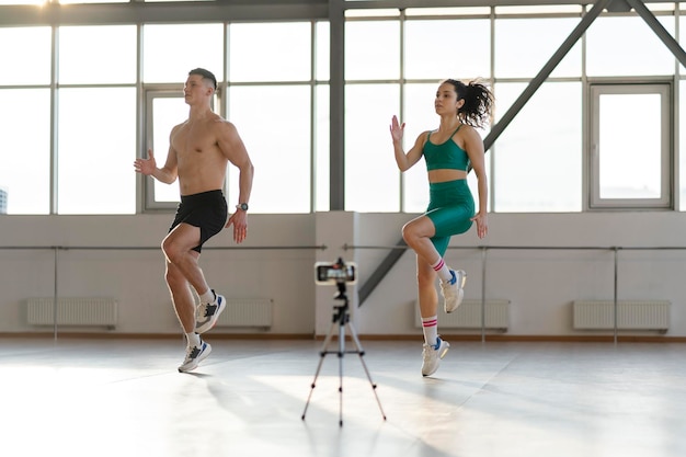 Hombre hispano musculoso y hermosa chica haciendo ejercicio en el gimnasio blogueando grabando video en línea