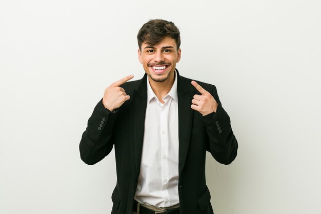 Foto hombre hispano de negocios joven sonríe, señalando con el dedo a la boca.