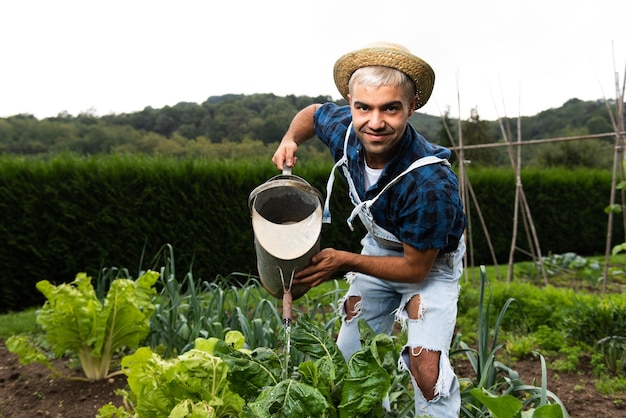 Hombre hispano regando verduras en un jardín mientras mira a la cámara.