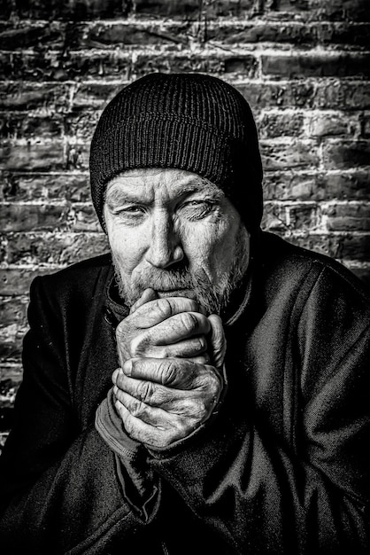 Foto hombre sin hogar en blanco y negro contra una pared de ladrillo calentando las manos