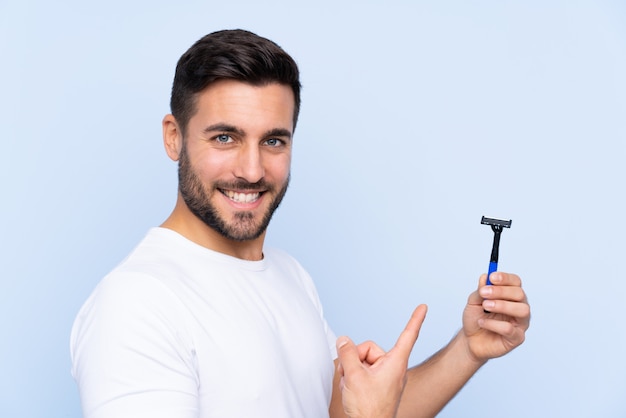 Hombre con hoja de afeitar sobre pared azul aislado