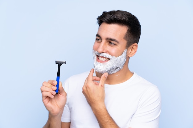 Hombre con hoja de afeitar sobre pared azul aislado