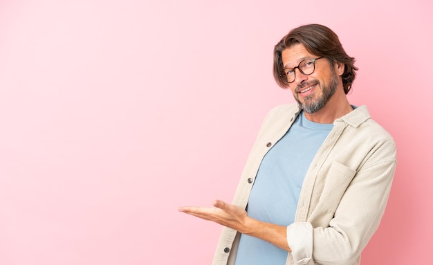 Hombre holandés mayor aislado de fondo rosa que presenta una idea mientras mira sonriendo hacia
