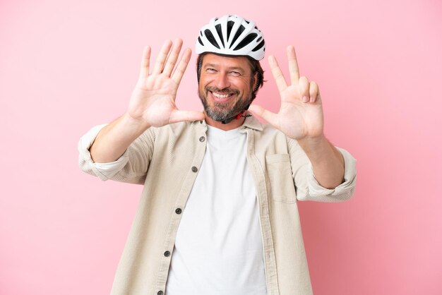 Hombre holandés mayor con casco de bicicleta aislado sobre fondo rosa contando ocho con los dedos