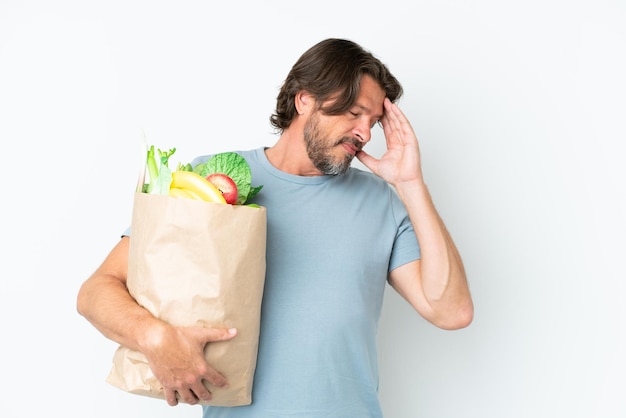Hombre holandés mayor sosteniendo una bolsa de compras sobre un fondo aislado con dolor de cabeza