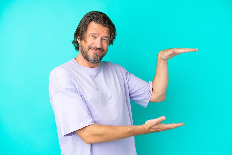 Foto hombre holandés senior aislado sobre fondo azul sosteniendo copyspace para insertar un anuncio