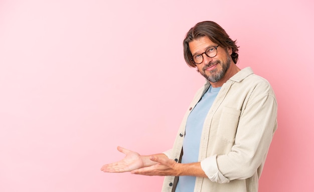 Hombre holandés senior aislado sobre fondo rosa extendiendo las manos hacia el lado para invitar a venir