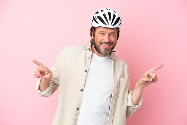 Foto hombre holandés senior con casco de bicicleta aislado sobre fondo rosa dedo acusador hacia los laterales y feliz