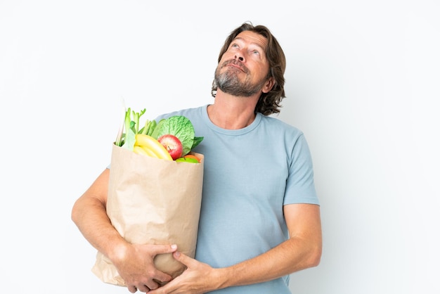 Hombre holandés senior sosteniendo la bolsa de la compra sobre fondo aislado y mirando hacia arriba