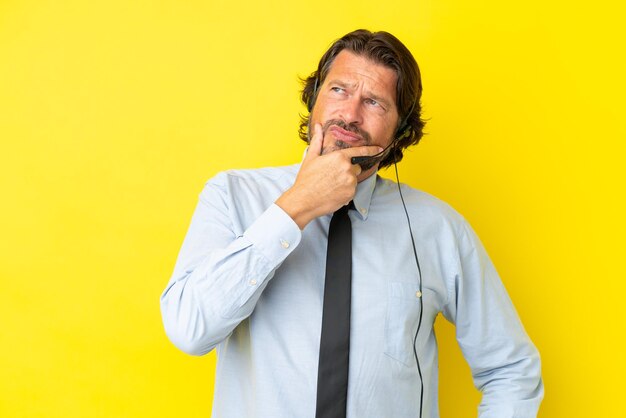 Hombre holandés telemarketer que trabaja con un auricular aislado sobre fondo amarillo que tiene dudas y con expresión de la cara confusa