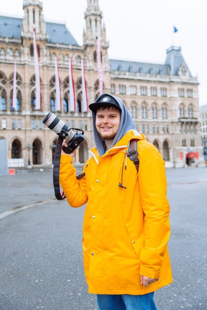Hombre con impermeable amarillo con cámara réflex digital grande en la plaza de la ciudad
