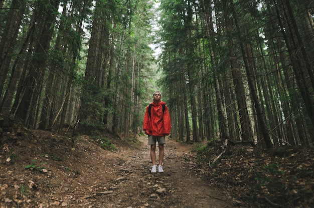 Hombre en un impermeable rojo se encuentra en un sendero en las montañas