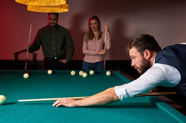 Hombre inclinado sobre la mesa mientras juega al billar, está concentrado en el juego, teniendo tiempo libre