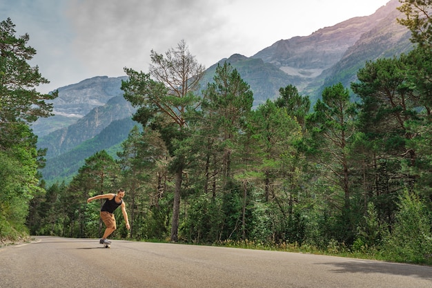 Hombre inconformista largo embarque en una carretera de montaña con curvas