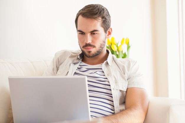 Hombre inconformista que usa la computadora portátil en el sofá