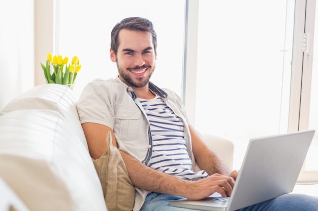 Hombre inconformista que usa la computadora portátil en el sofá
