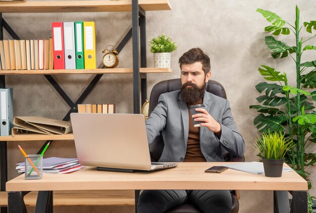 El hombre independiente concentrado usa la comunicación informática en línea en la oficina con correo electrónico de cheque de café