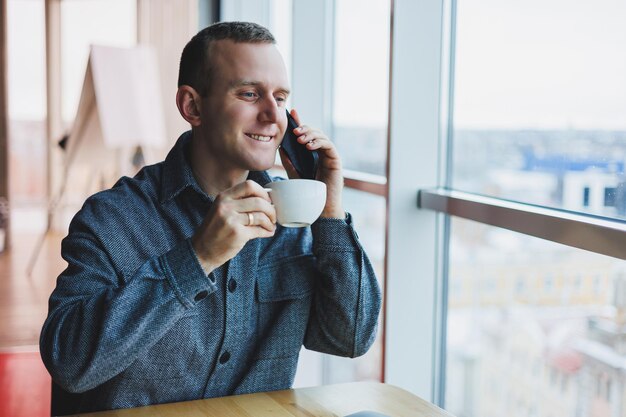 Hombre independiente europeo revisando la notificación en el teléfono inteligente sobre transacciones de dinero haciendo negocios en línea trabajando de forma remota mientras está en un café y bebiendo café