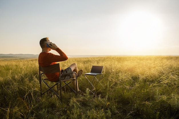 Hombre independiente hablando por teléfono y trabajando en línea usando una computadora portátil y disfrutando de la vista de la naturaleza al atardecer Concepto de trabajo remoto