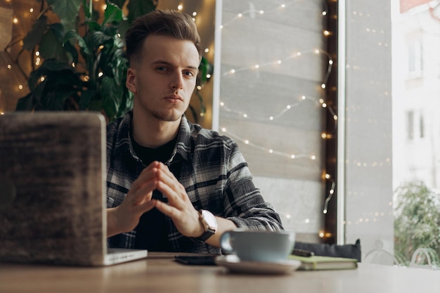 hombre independiente mirando la cámara mientras se sienta en la mesa con una computadora portátil durante el trabajo en el café