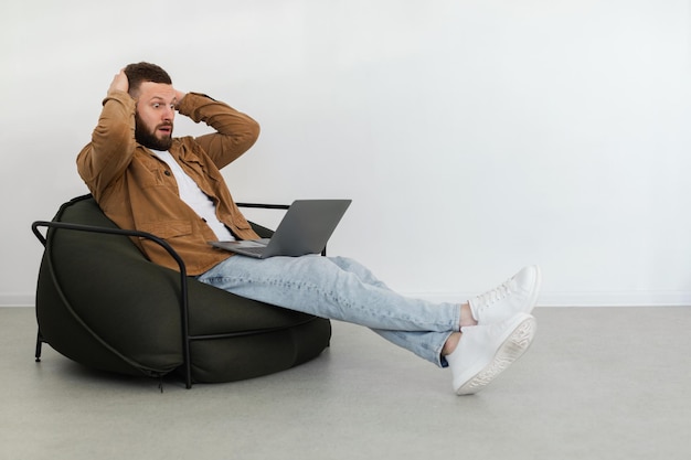 Hombre independiente mirando la computadora portátil en estado de shock tocando la cabeza en el interior