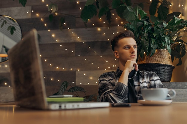 hombre independiente pensando en el proyecto mientras se sienta en la mesa con una computadora portátil durante el trabajo remoto en el café