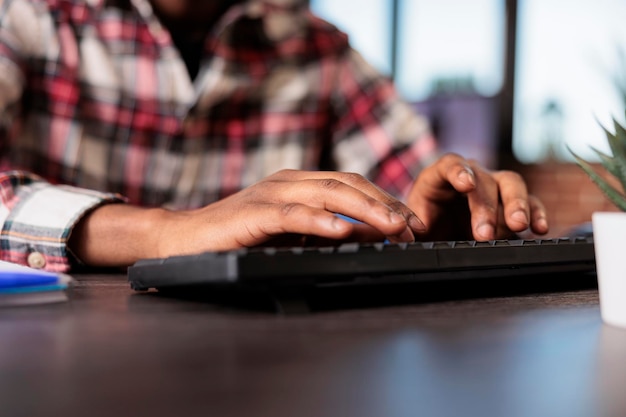 Foto hombre independiente que navega por internet en la computadora, escribe un informe en línea en el escritorio de su casa y envía correos electrónicos. trabajando en un trabajo remoto con una empresa independiente, usando una pc para hacer archivos de papeleo. de cerca.