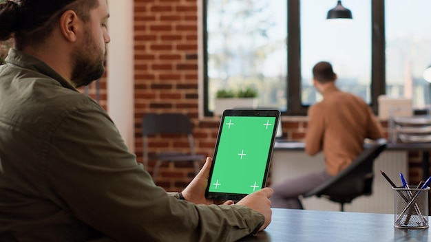 Hombre independiente que sostiene una tableta digital con pantalla verde, mirando el fondo de la clave de croma en blanco. Análisis de la plantilla de espacio de copia aislada en la pantalla del dispositivo, escritorio de la oficina de la empresa.