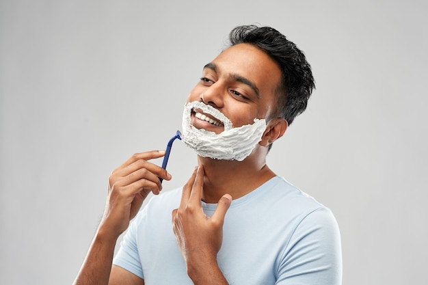 Foto hombre indio afeitando la barba con una hoja de afeitar