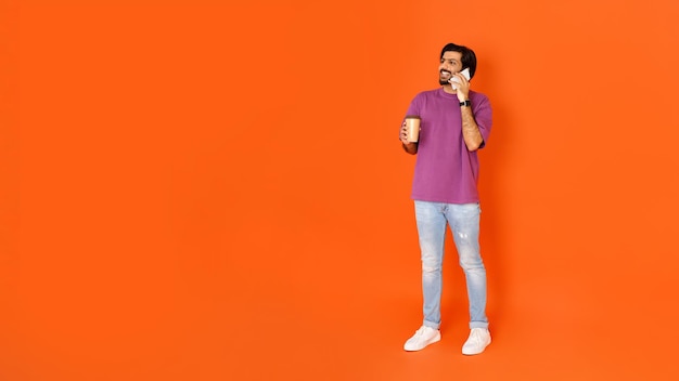 Hombre indio alegre que usa un teléfono inteligente tiene una llamada telefónica bebiendo café