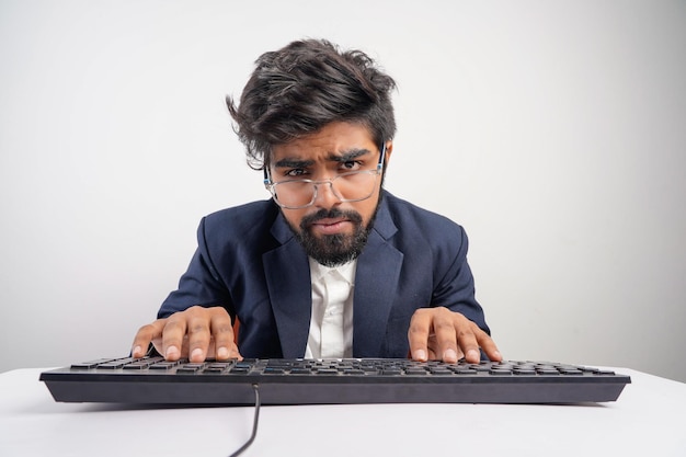 Hombre indio con anteojos trabajando en la computadora con las manos sobre el teclado mientras escribe aislado en fondo blanco Vista frontal