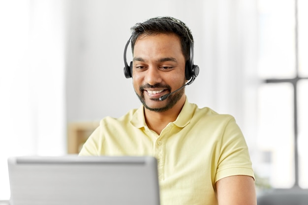 hombre indio con auriculares y portátil trabajando en casa
