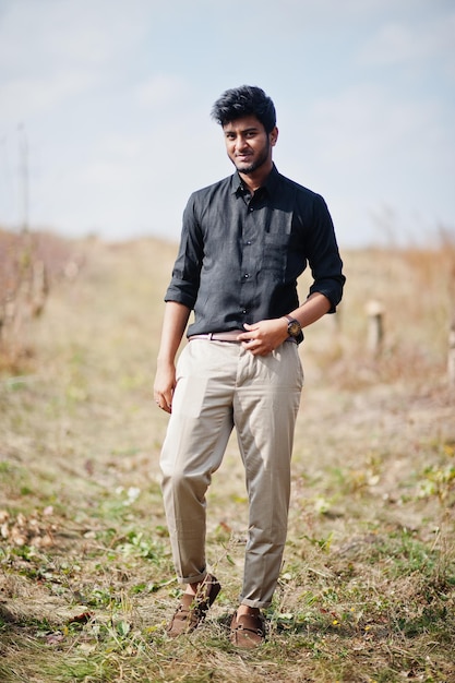 Hombre indio con camisa negra y pantalones beige posados en el campo