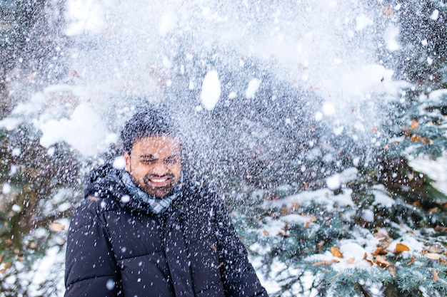 Hombre indio disfrutando de los copos de nieve cayendo desde arriba en el bosque