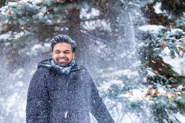 Hombre indio disfrutando de los copos de nieve cayendo desde arriba en el bosque