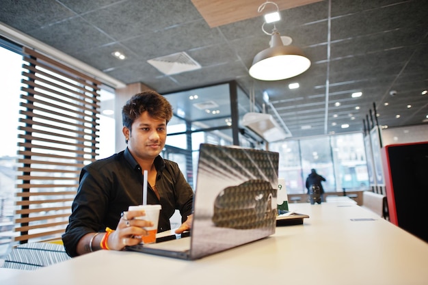 Hombre indio elegante sentado en un café de comida rápida contra su computadora portátil