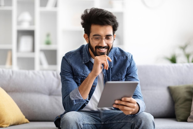 Hombre indio enfocado con gafas usando una tableta digital en casa