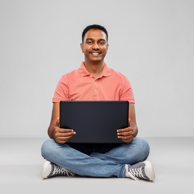 hombre indio feliz con computadora portátil en el suelo