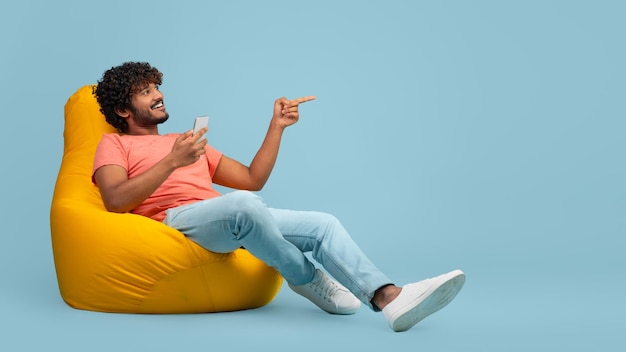 Hombre indio feliz con teléfono inteligente apuntando al espacio de copia