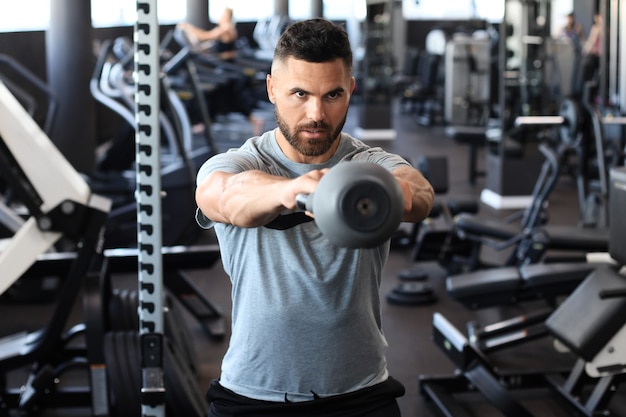 Hombre indio en forma y musculoso se centró en levantar una pesa durante una clase de ejercicios en un gimnasio.