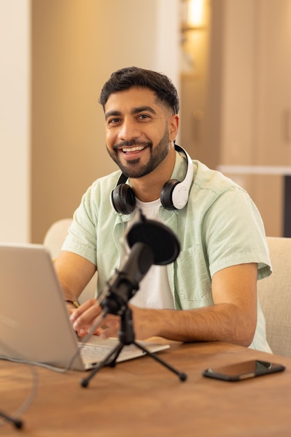 Hombre indio grabando podcast en una oficina casera moderna con micrófono portátil y auriculares