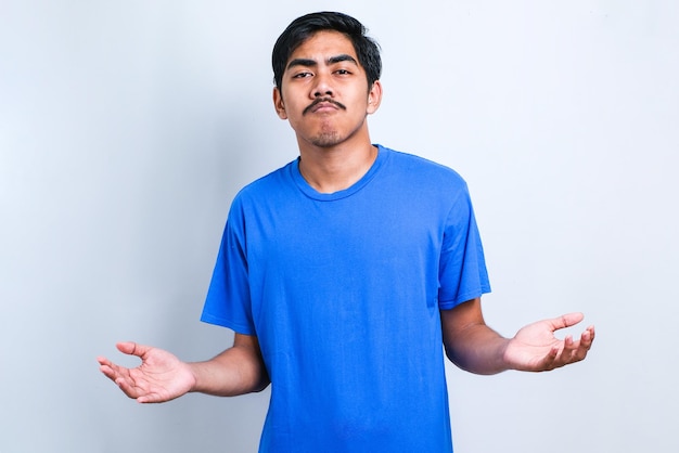 Hombre indio guapo joven con camisa casual sobre fondo blanco expresión desorientada y confusa con los brazos y las manos levantadas. Concepto de duda.