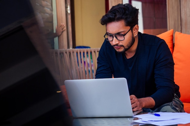 Hombre indio guapo y joven exitoso que trabaja de forma independiente navegando a distancia con una computadora portátil