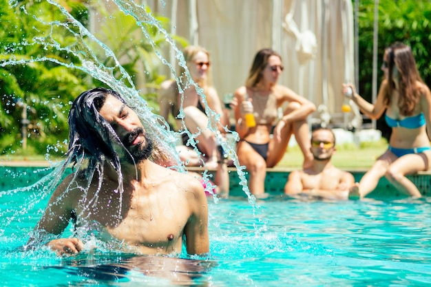 Hombre indio guapo de pelo largo y húmedo con gafas de sol rosas, fondo de amigos felices, estado de ánimo relajado