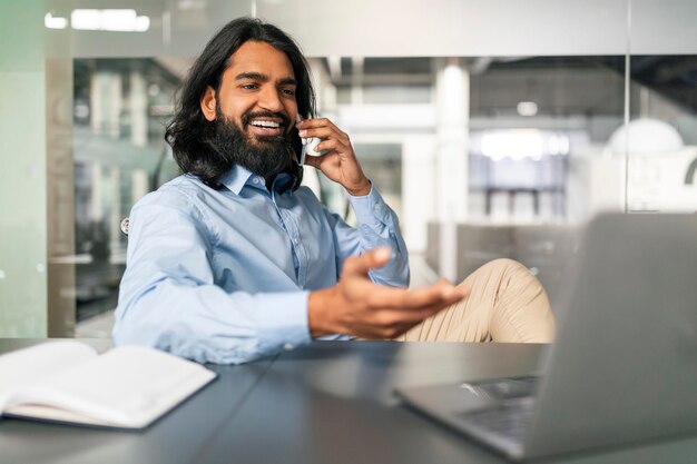 Hombre indio hablando por teléfono móvil trabajando en la computadora en la oficina