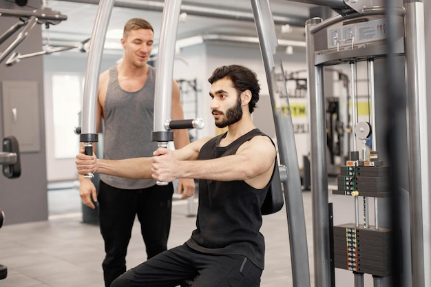 Hombre indio haciendo ejercicios en equipos especiales en el gimnasio con entrenador personal